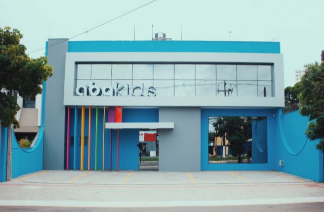 Fachada da unidade de intervenção precoce da clínica Abakids, prédio moderno azul e cinza com letreiro colorido na entrada, fotografia realista de arquitetura externa