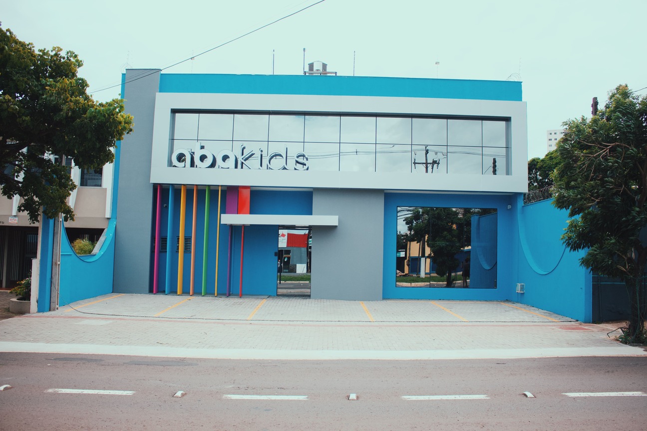 Fachada da clínica Abakids, prédio moderno azul com letreiro colorido e entrada envidraçada, fotografia realista de arquitetura externa