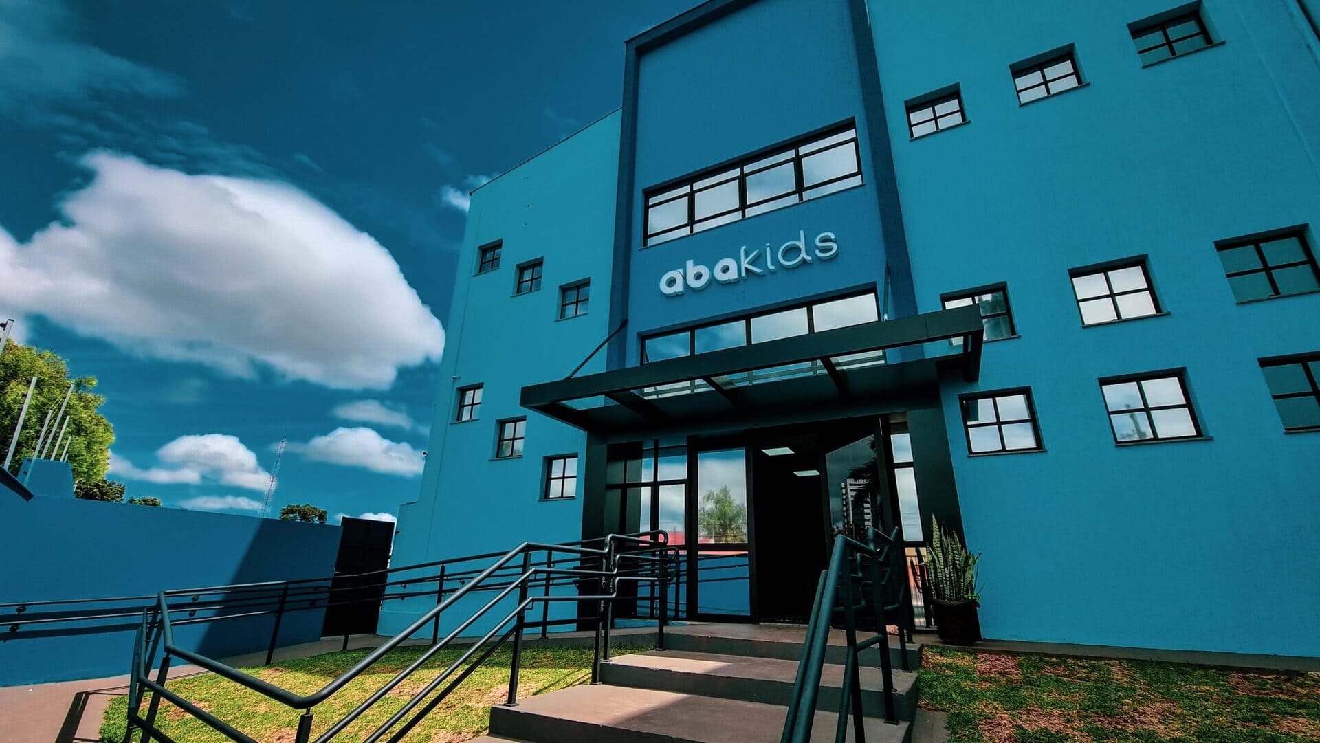 Fachada da unidade de intervenção continuada da clínica Abakids, prédio azul moderno com letreiro iluminado e entrada envidraçada, fotografia realista de arquitetura externa em ângulo